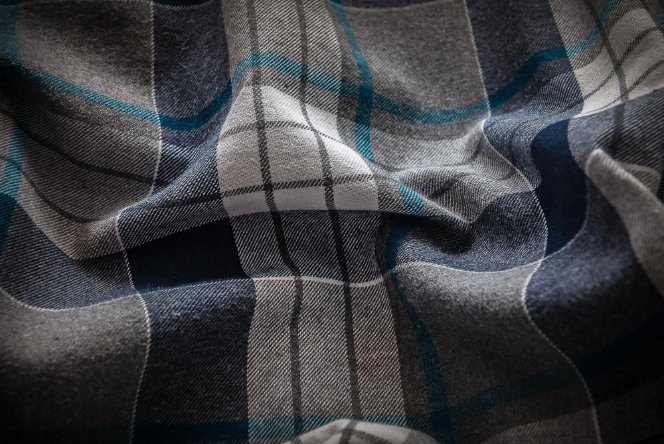 A close-up view of dark plaid flannel fabric with blue and grey tones.