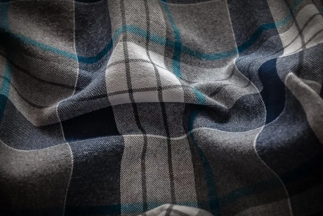 A close-up view of dark plaid flannel fabric with blue and grey tones.