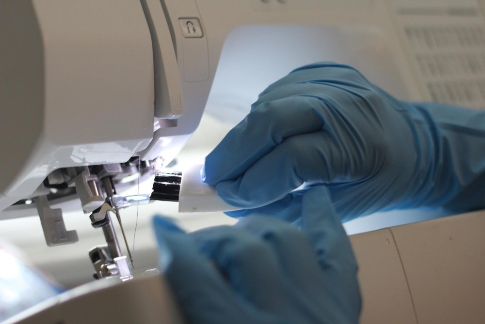 Person wearing blue gloves cleaning and maintaining the needle area of a sewing machine.