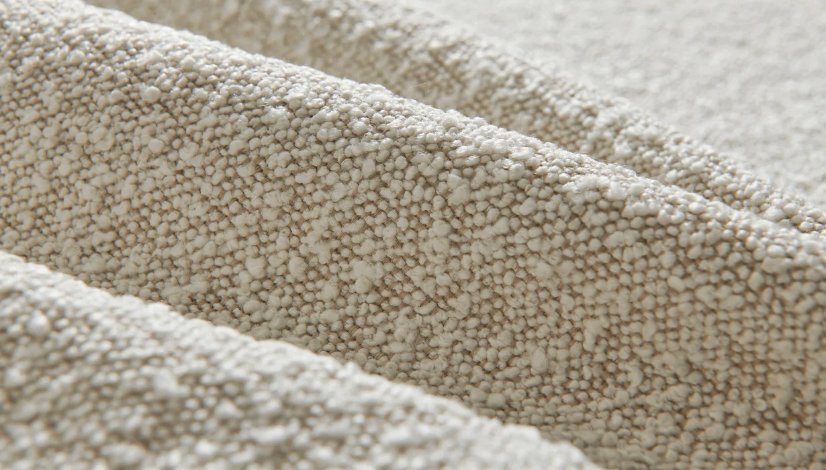 Close-up texture of soft beige bouclé fabric showing its signature looped and nubby surface.