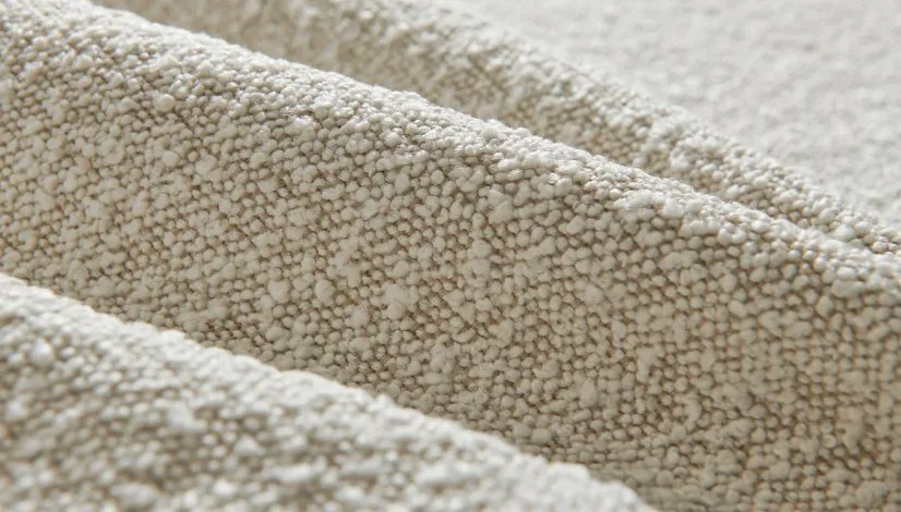Close-up texture of soft beige bouclé fabric showing its signature looped and nubby surface.