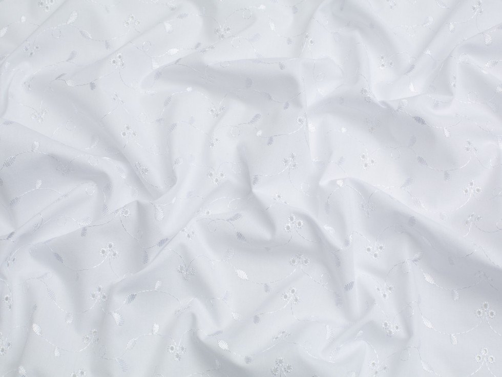 Close-up of white Broderie Anglaise cotton fabric with delicate embroidered floral patterns.