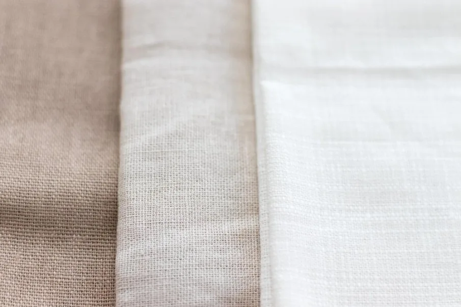 Close-up view of three types of cambric cotton fabric in beige and white tones.