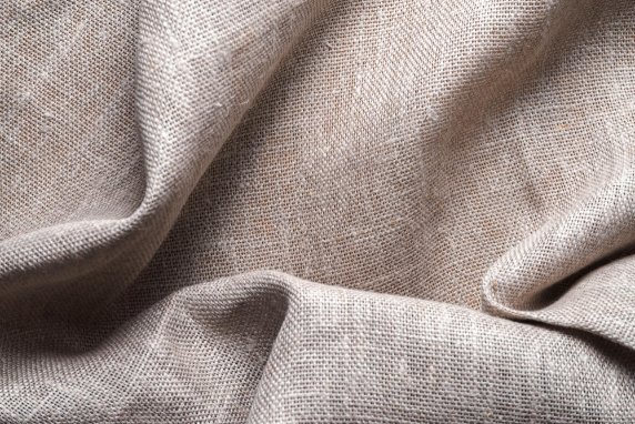 Textured cambric linen fabric in neutral beige tone, showing detailed weave and natural folds.