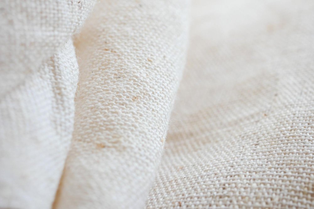 Close-up texture of unbleached cheesecloth cotton fabric with visible open weave.