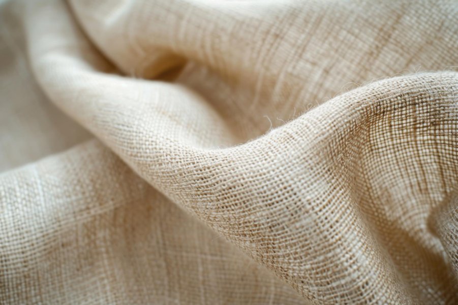 Close-up of beige loose weave linen fabric with visible threads and soft folds.