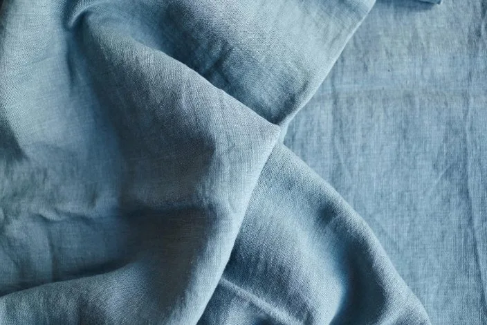Close-up of blue stonewashed linen fabric texture showing natural wrinkles and soft, breathable weave characteristic of quality linen sheets