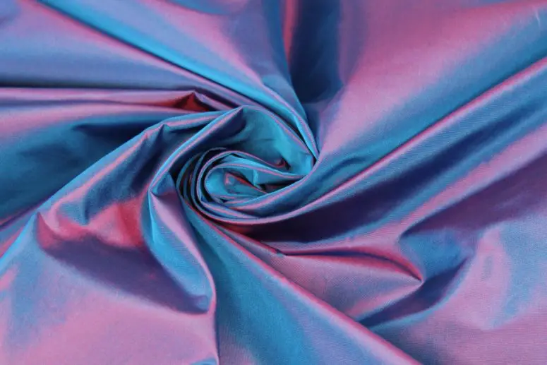 Shiny iridescent acetate taffeta fabric in blue and pink tones with a swirling drape