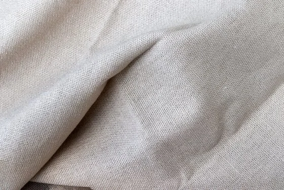 Close-up of natural beige Belgian linen fabric showing its woven texture and organic fibers.