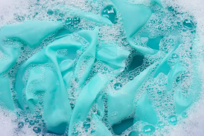 Close up of turquoise fabric soaking in soapy water with visible detergent bubbles