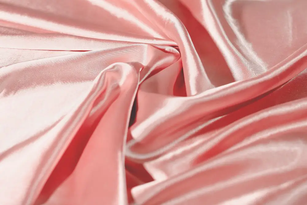 Soft pink satin fabric with a glossy finish draped in flowing folds.