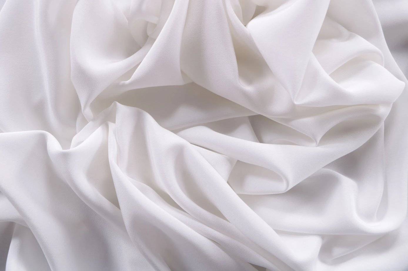 White Crepe de Chine fabric displayed in flowing folds to show drape and fluid movement.