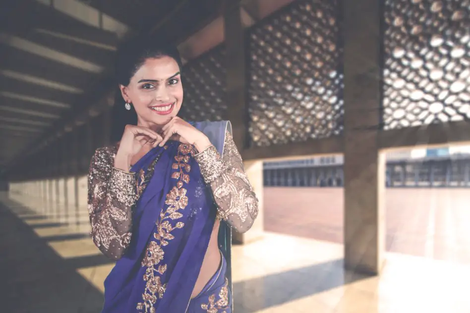 Woman wearing a blue Eri silk saree with golden embroidery in a contemporary architectural setting