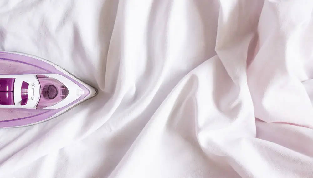 Purple steam iron resting on white satin fabric during garment care