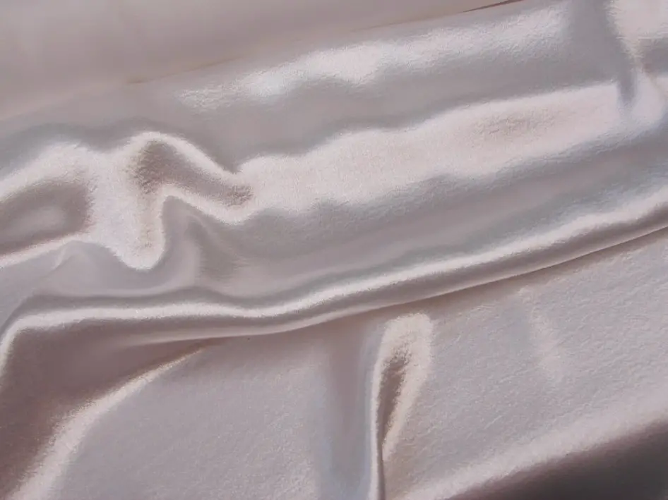 Close up of light pink polyester crepe back satin fabric showing its glossy surface and smooth drape