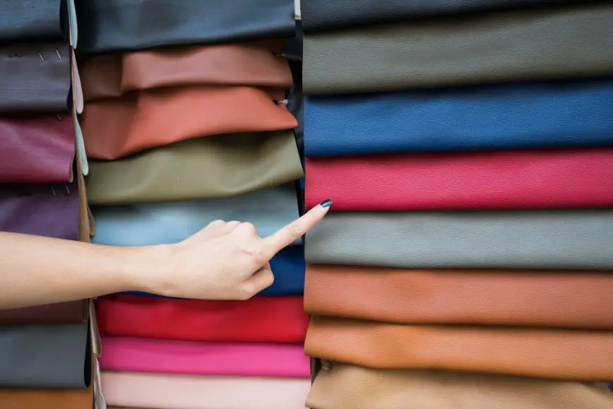 Hand pointing toward colorful fabric rolls in a shop for satin selection