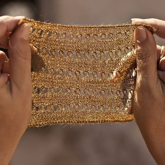 Hands holding a knitted sea silk fabric swatch showing its fine texture and golden color