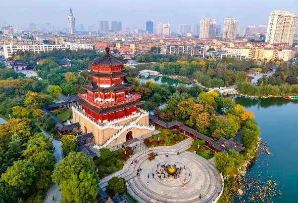 Aerial view of a traditional Chinese pagoda surrounded by trees, lakes, and modern city buildings in Shandong Province