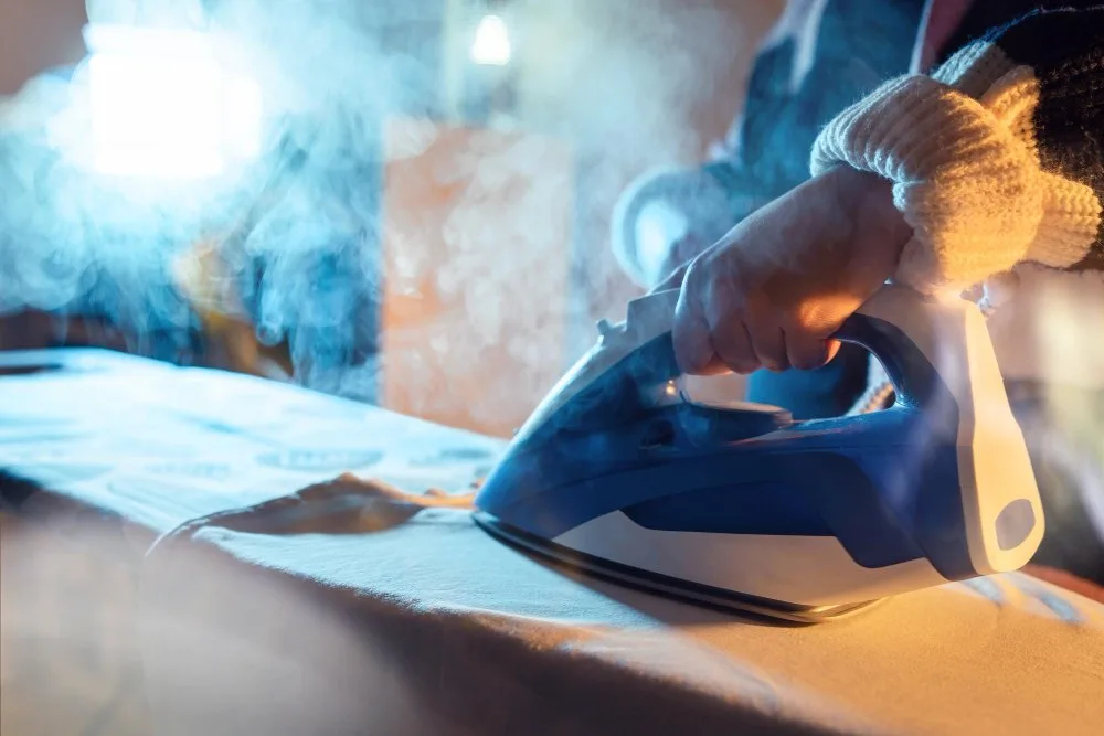 Person using a steam iron on a garment with visible steam rising during fabric care