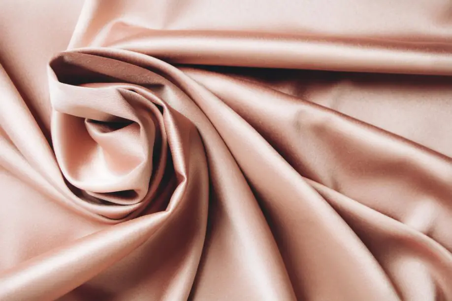 Smooth peach coloured charmeuse silk fabric with glossy folds and a flowing drape