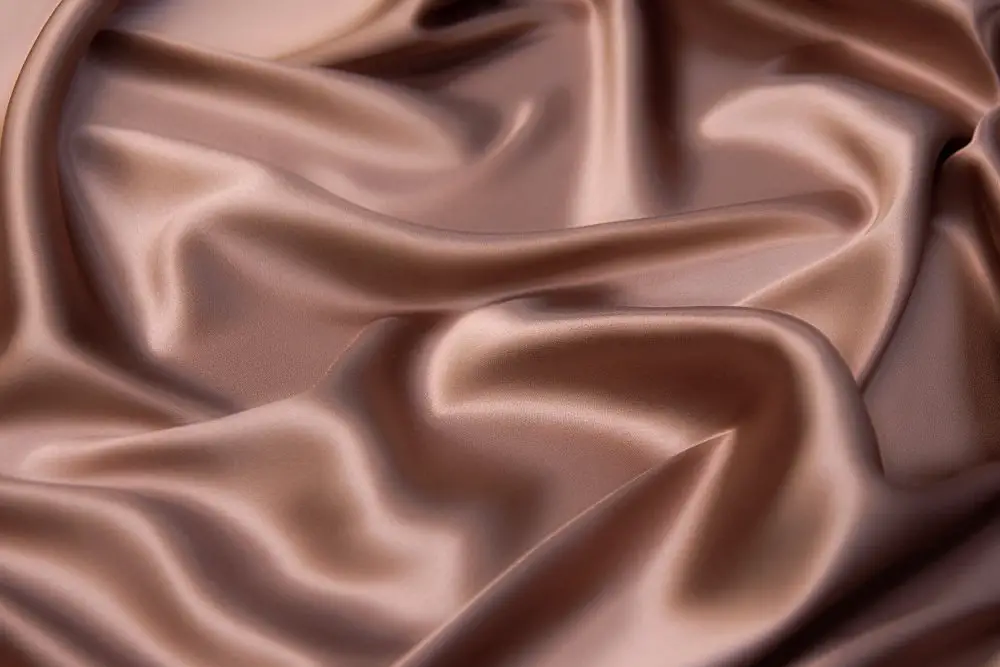 Rich brown silk crepe back satin fabric draped in luxurious folds with a soft glossy surface
