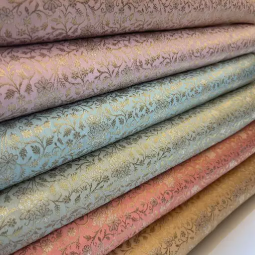 Stacks of synthetic brocade fabrics in pastel shades with metallic floral designs