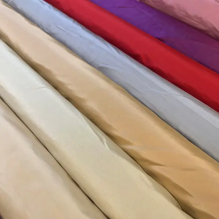 Rolls of taffeta fabric in various colors including gold, red, purple, and pastel shades