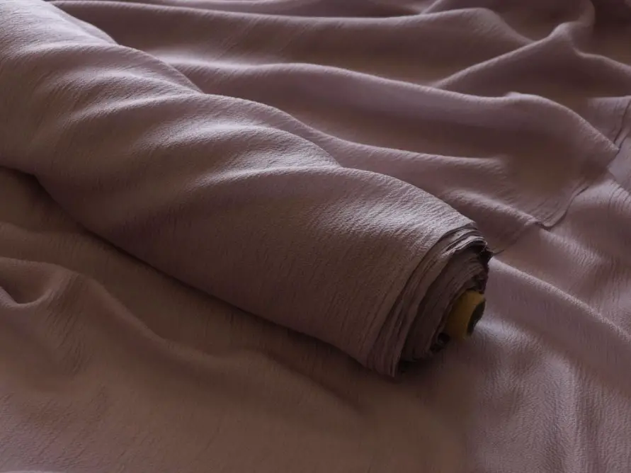 Roll of crepe georgette fabric in soft mauve color showing textured surface and flowing drape
