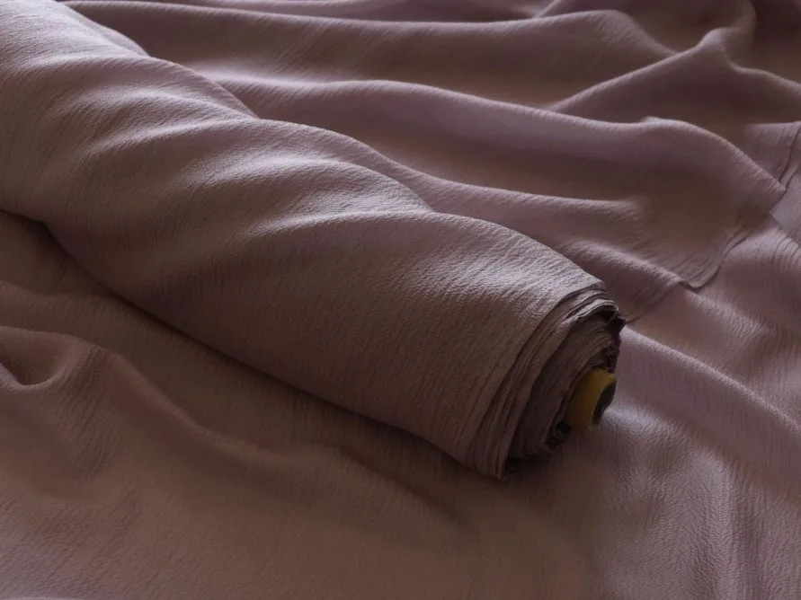 Roll of crepe georgette fabric in soft mauve color showing textured surface and flowing drape.