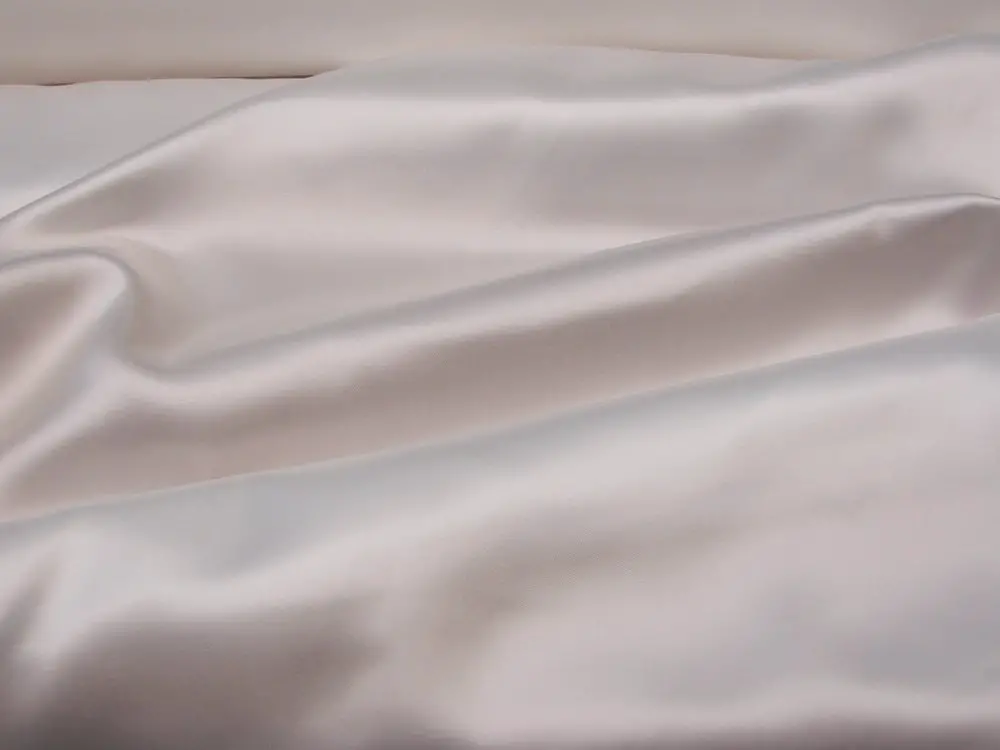 Cream colored acetate satin fabric draped in smooth folds showing its glossy surface and elegant texture