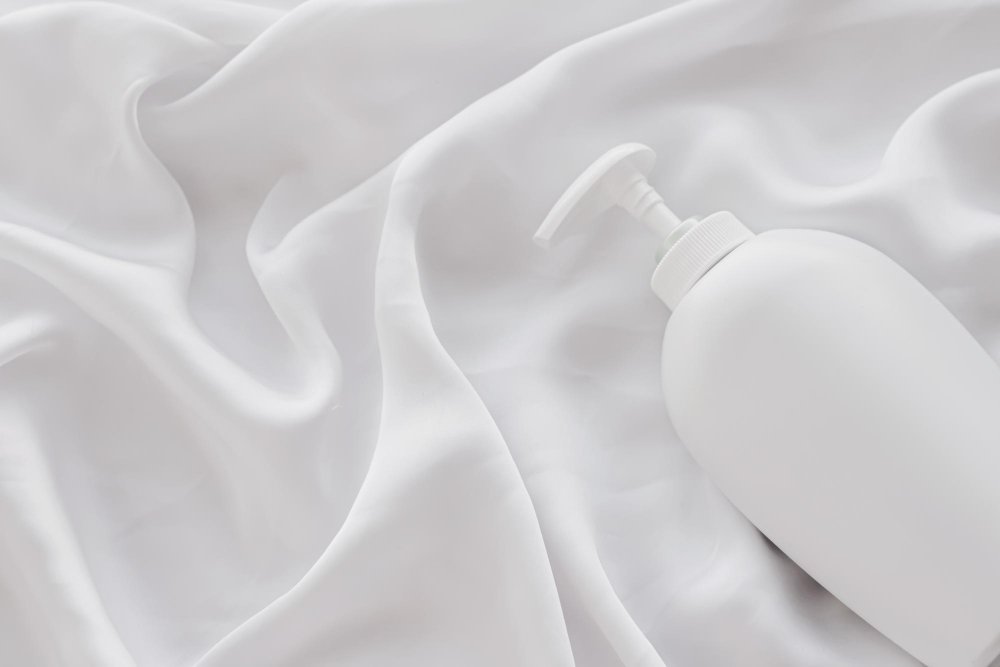 White bottle of fabric care product placed on white acetate satin fabric to represent cleaning and maintenance steps