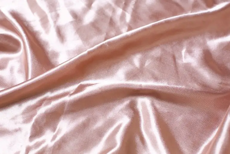 Close up of pale pink satin fabric showing smooth weave and soft reflective sheen