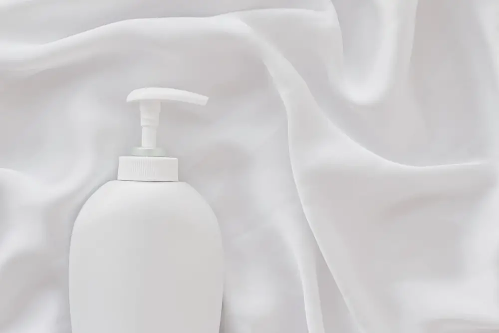 Laundry detergent bottle placed on white satin blend fabric to represent fabric care