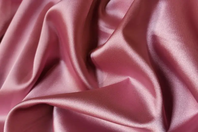 Soft pink charmeuse satin fabric draped in folds showing its lustrous surface