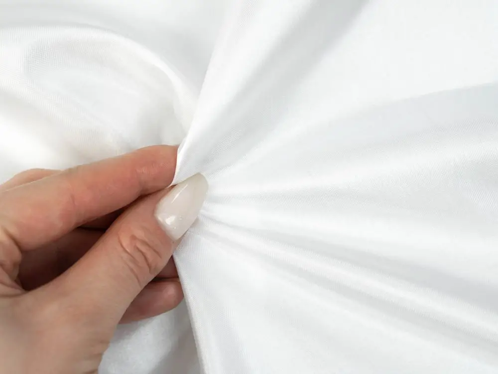 Hand holding white satin silk fabric to show its smooth texture, natural sheen and fine weave