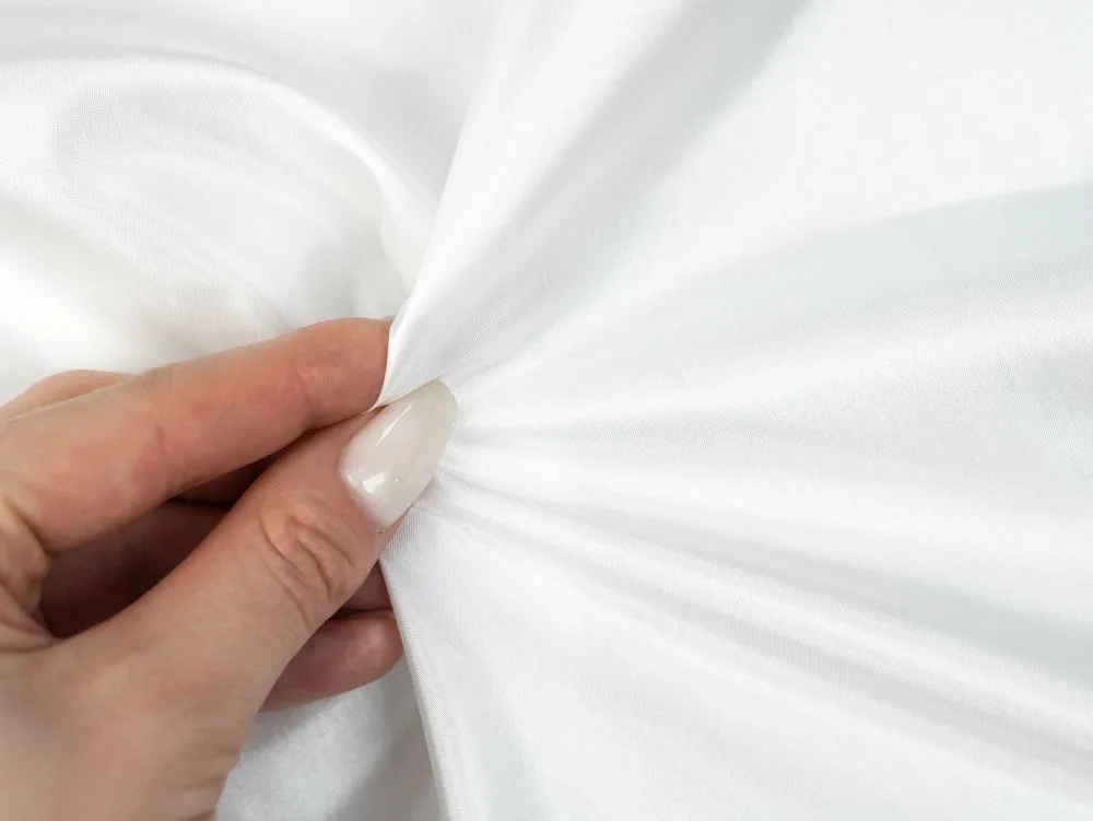 Hand holding white satin silk fabric to show its smooth texture, natural sheen and fine weave