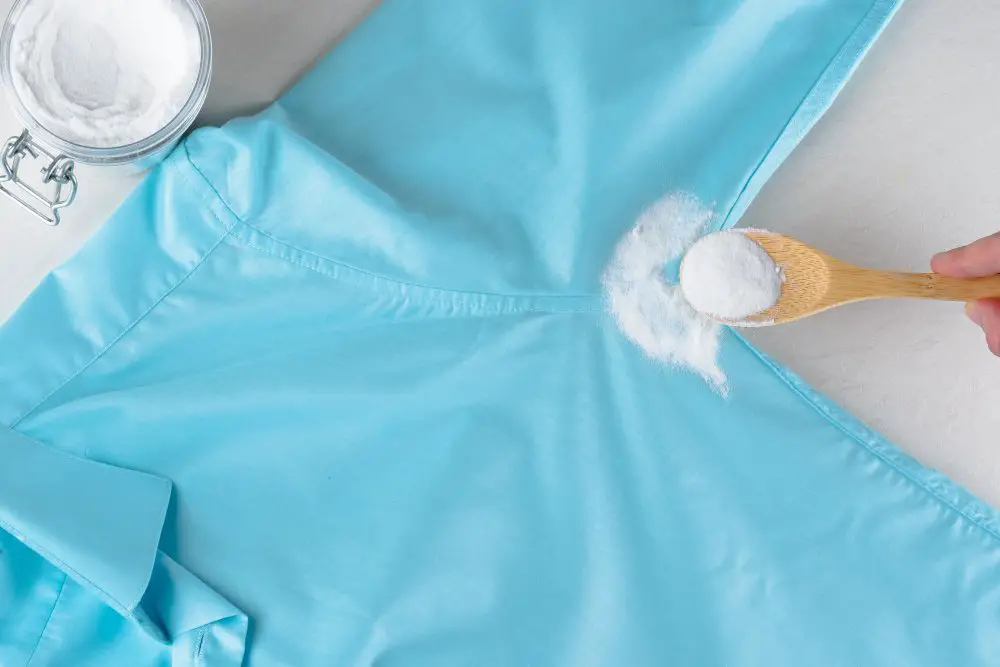 Blue acetate garment being treated with white cleaning powder applied to a stain using a wooden spoon