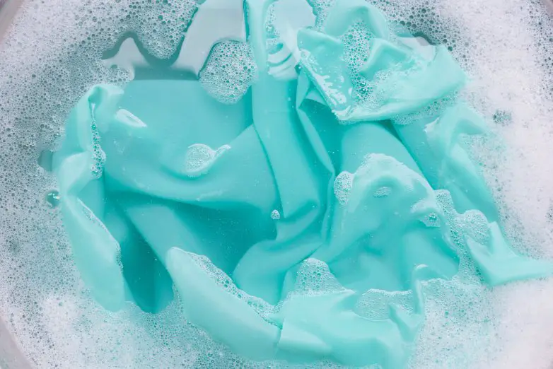 Aqua panne satin fabric soaking in a basin of soapy water during gentle hand washing