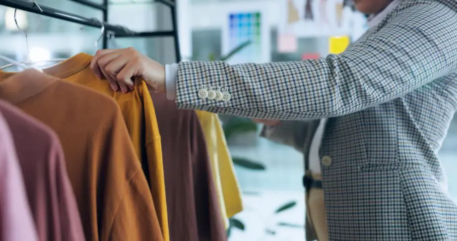 Person browsing camel wool coats on a clothing rack