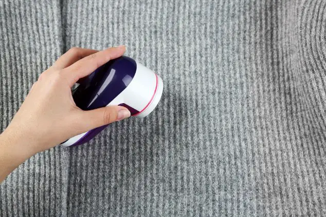 Hand using a fabric shaver to remove pilling from a grey cashmere sweater