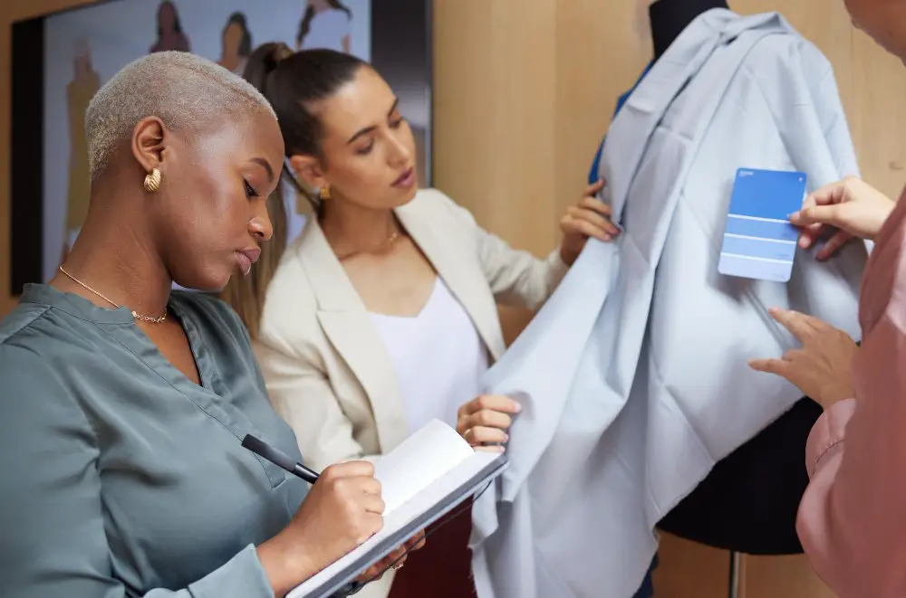 Two women examining a draped fabric on a mannequin while comparing notes and a color swatch
