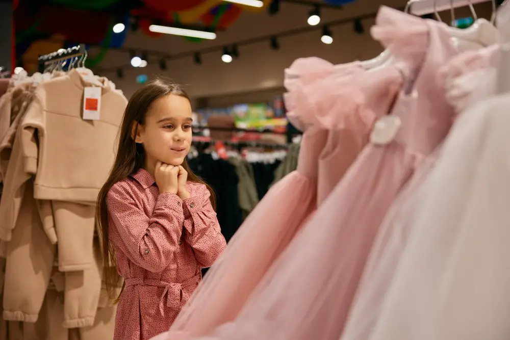 Young girl smiling while choosing a formal dress in a clothing store
