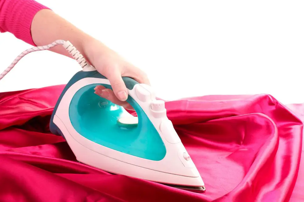 Hand ironing bright pink Monroe satin fabric using a low heat steam iron