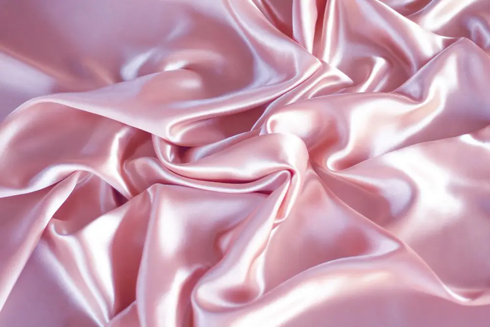 Pink polyester charmeuse satin draped in soft folds showing its reflective sheen and lightweight drape