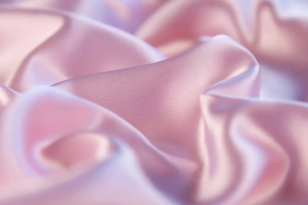 Soft pink rayon charmeuse fabric draped in gentle folds showing its smooth texture and elegant sheen
