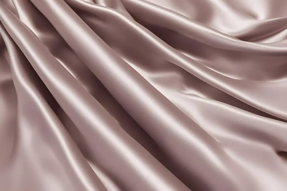 Taupe silk charmeuse fabric draped in elegant waves showing its glossy surface and luxurious smoothness