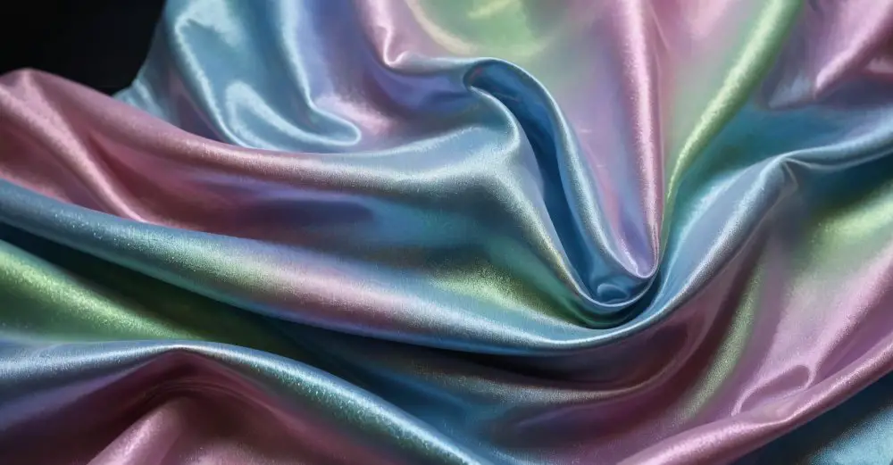 Iridescent baronet satin fabric in shades of blue, pink, and green draped in soft folds