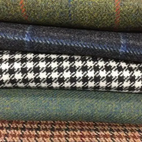 Various tweed fabrics stacked together showing different weights, patterns, and colors