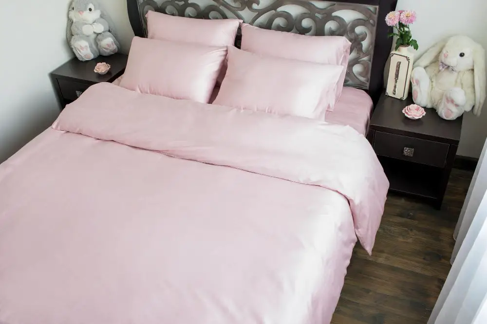 Pink charmeuse bedding set on a neatly made bed showing its smooth finish and elegant drape