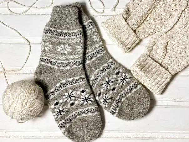 Hand knitted merino wool socks and gloves displayed with yarn on a wooden surface